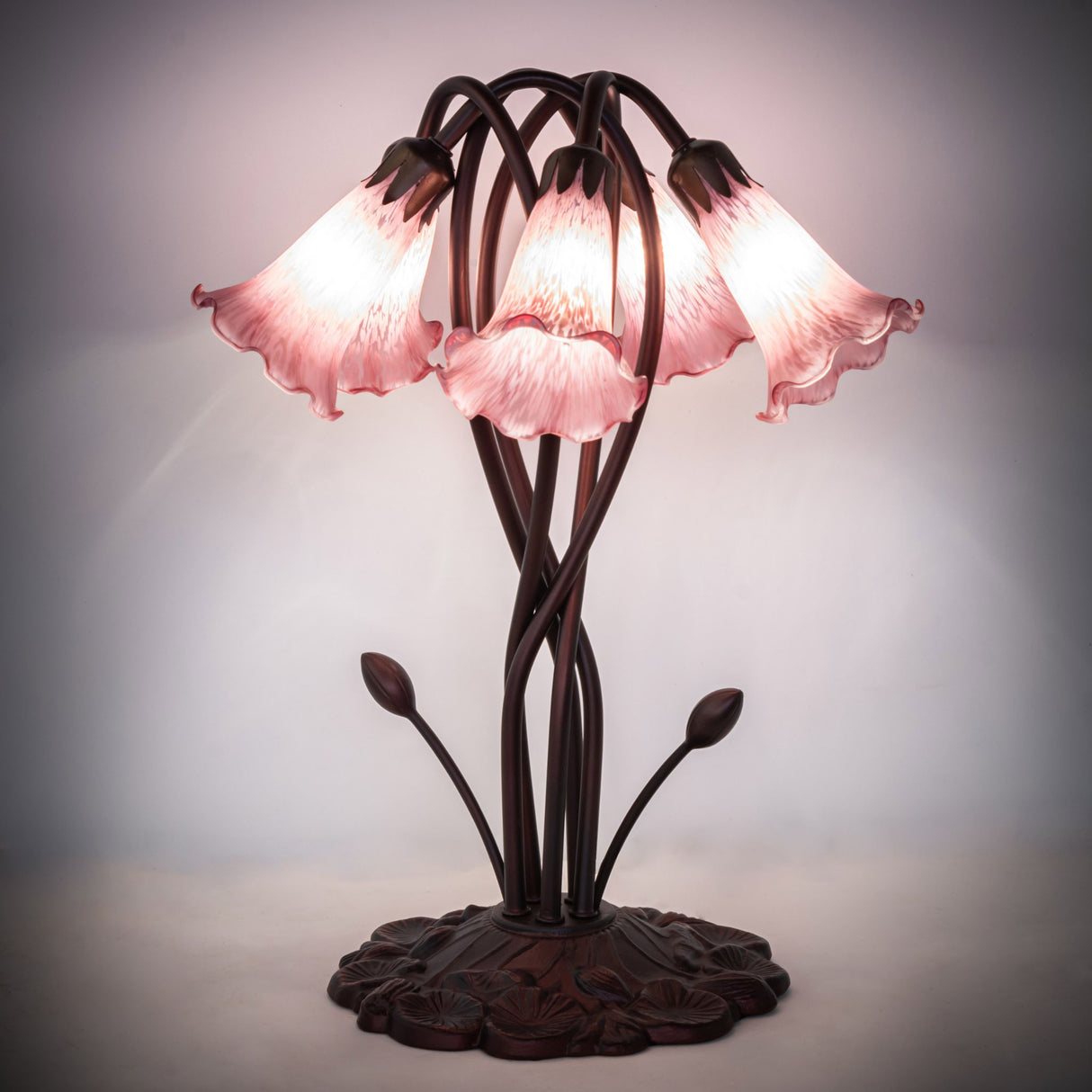 Illuminated lavender Tiffany pond lily table lamp in a dark setting.