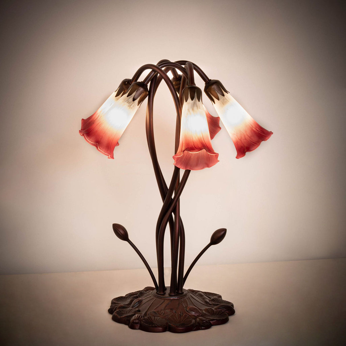 Warmly illuminated 17" pink and white pond lily lamp in a dimly lit setting.