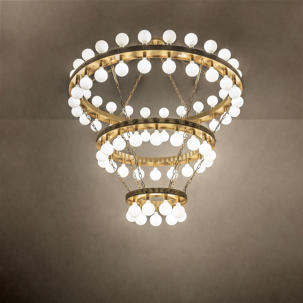 Ambient view of 75-light chandelier glowing in room setting with brushed brass rings.