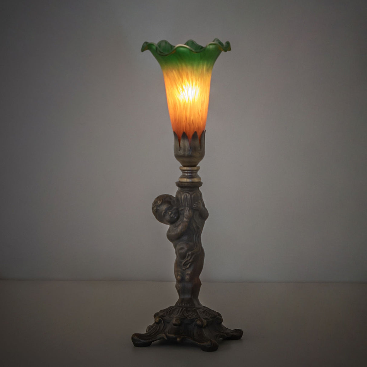 Amber and green pond lily mini lamp with cherub base in ambient lighting.