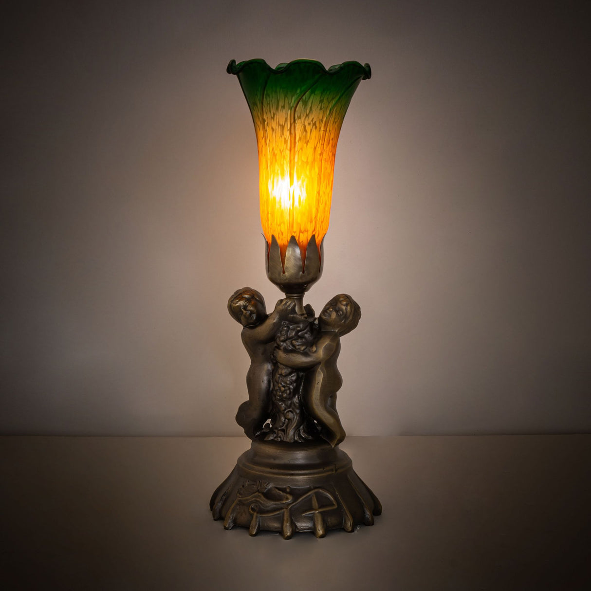 Amber and green Tiffany pond lily lamp glowing in ambient light setting.