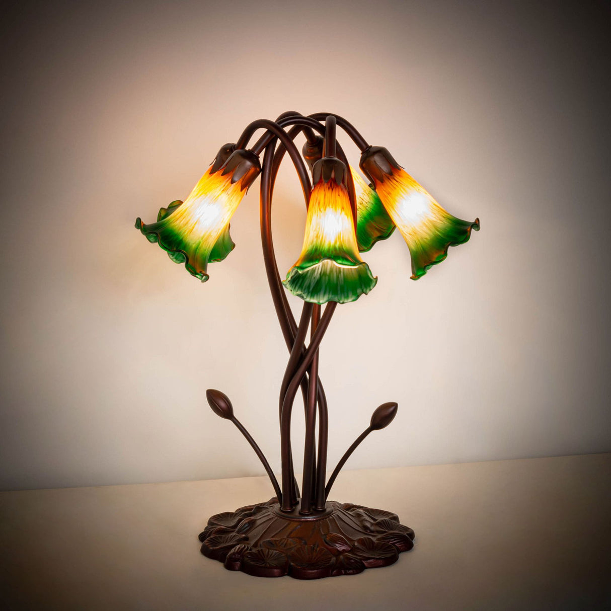 Illuminated amber and green Tiffany pond lily table lamp in a dark setting.