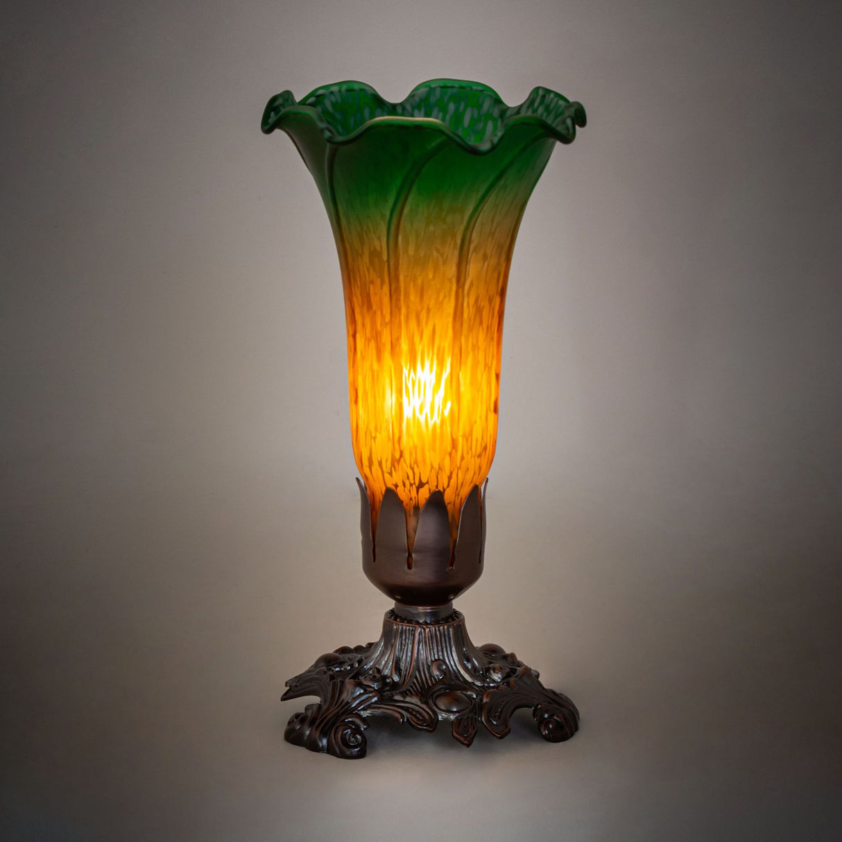 Amber and Green Tiffany Pond Lily lamp glowing in a dark setting.