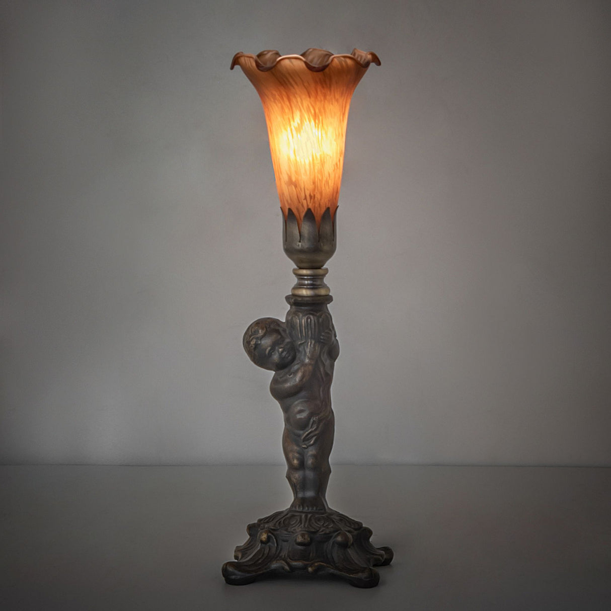 Amber Pond Lily Cherub Mini Lamp glowing warmly in a dimly lit setting.