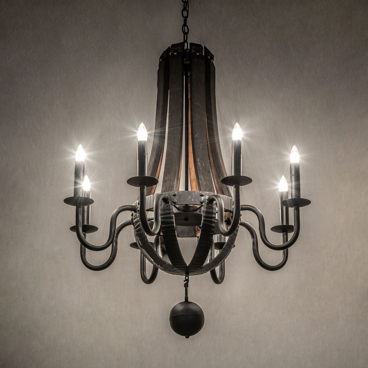 Ambient view of a chandelier with a warm glow from eight faux candles on rustic wood and black metal.