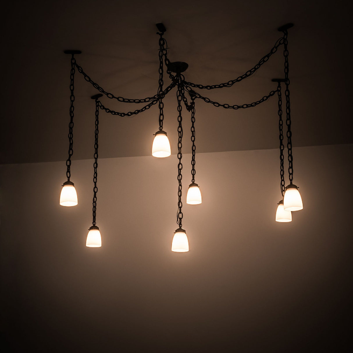 Castilian 7-light adjustable pendant illuminated, showcasing its ambient light effect in a room setting.