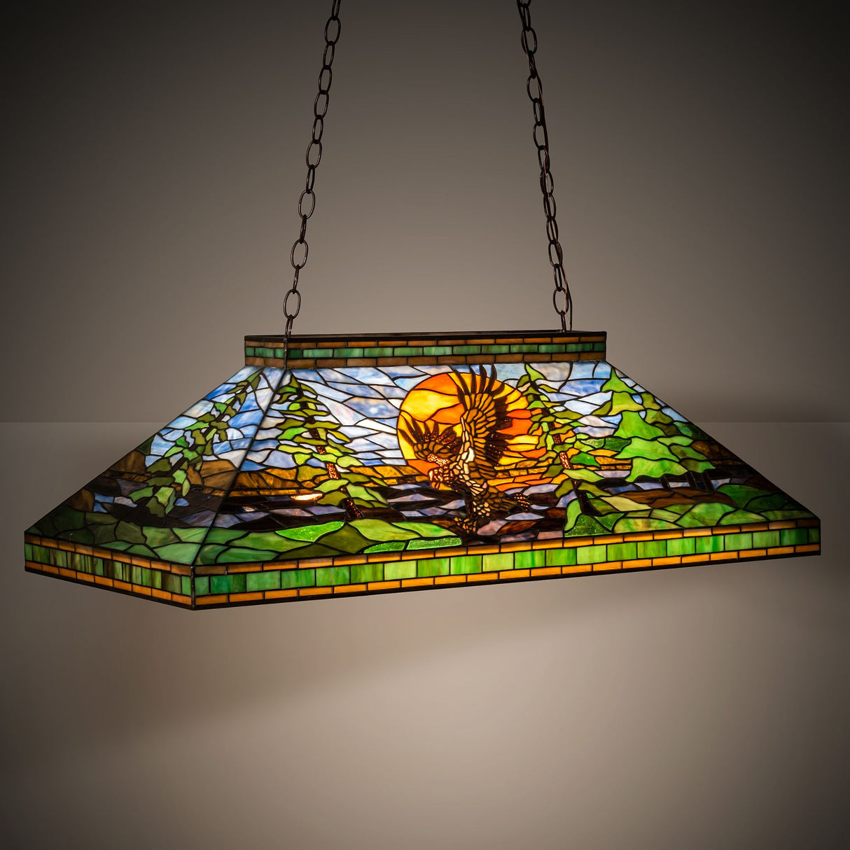 Illuminated view of the Eagle at Sunset pendant with a glowing woodland-themed art glass design.
