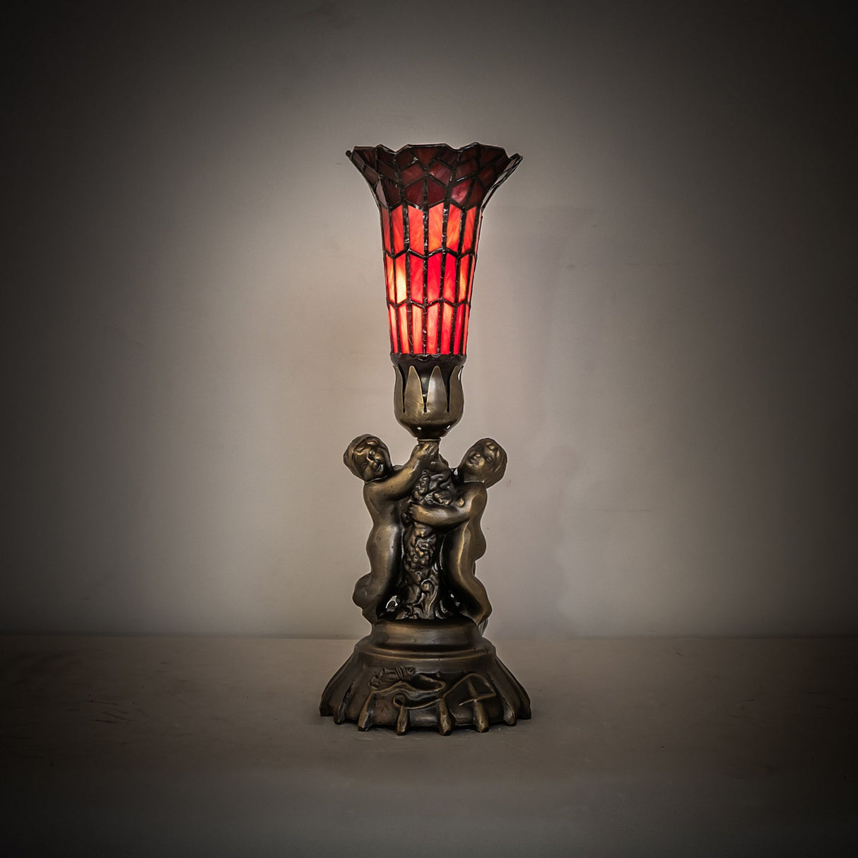 Glowing red pond lily lamp with twin cherub sculpture base on display.
