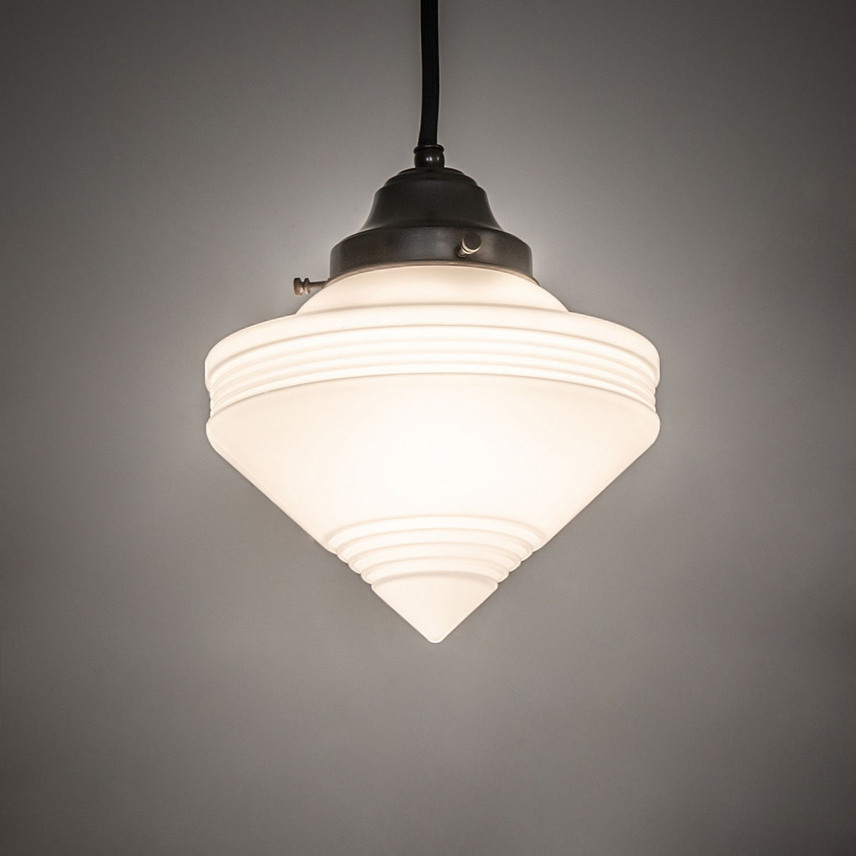 Illuminated mini pendant with deco cone shape against a dark background.