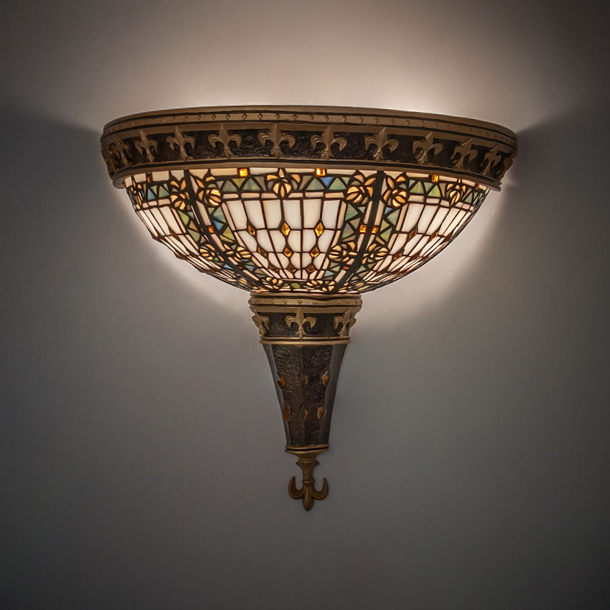 Illuminated Fleur-de-lis wall sconce casting a warm glow on a white wall.