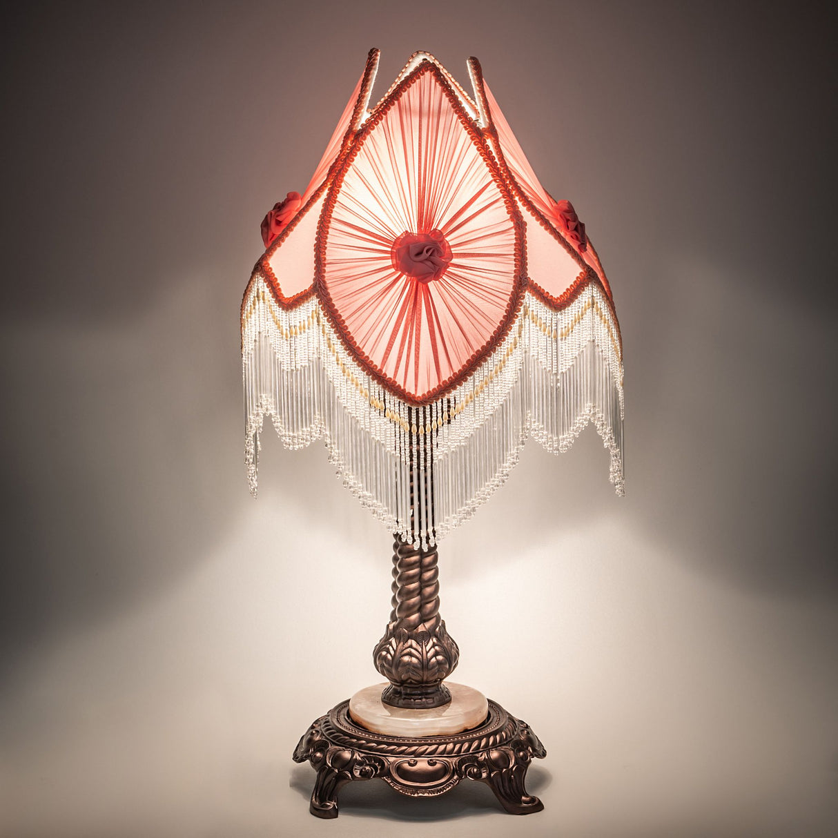 Illuminated pink fringe lamp with bronze base, showcasing intricate details.