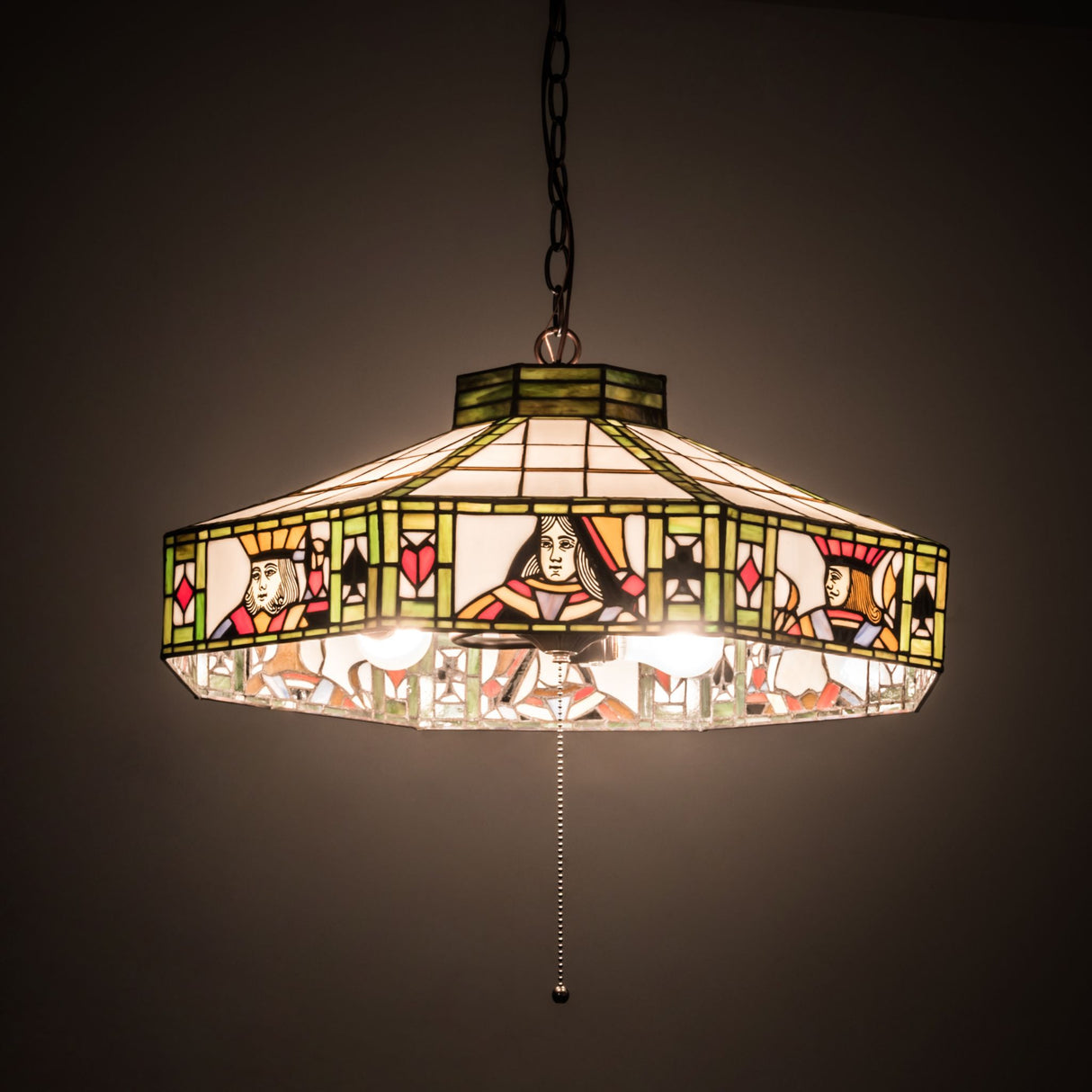 Illuminated Poker Face pendant casting light with its stained glass design.
