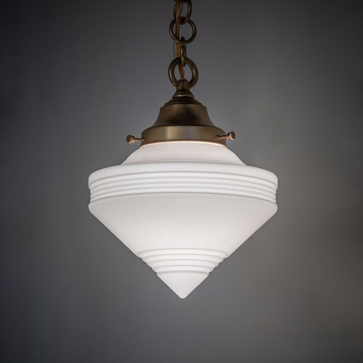 Lit brass pendant with ribbed white cone globe on display.