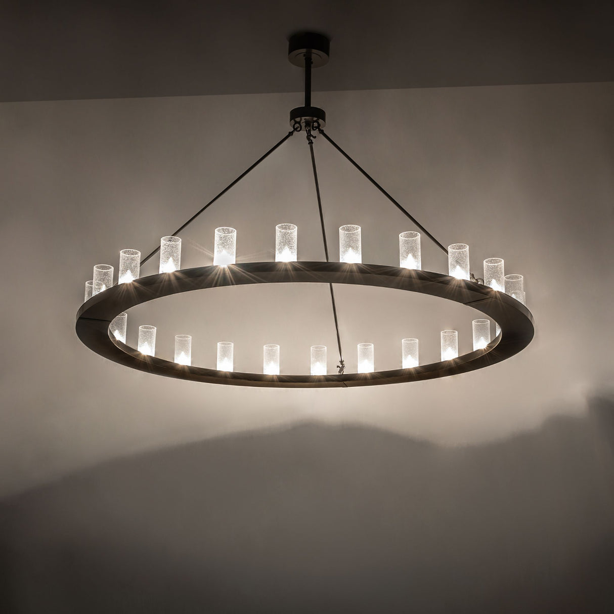 Loxley 24-light chandelier installed, glowing seeded glass cylinders creating warm ambient illumination.