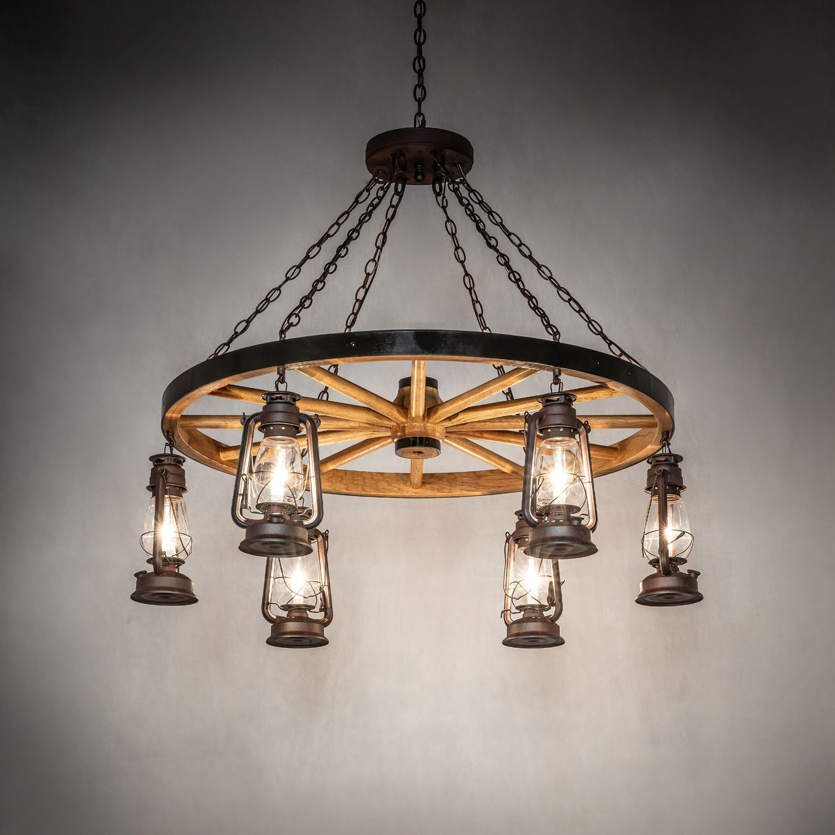 Miners Lantern wagon wheel chandelier illuminated in interior setting.
