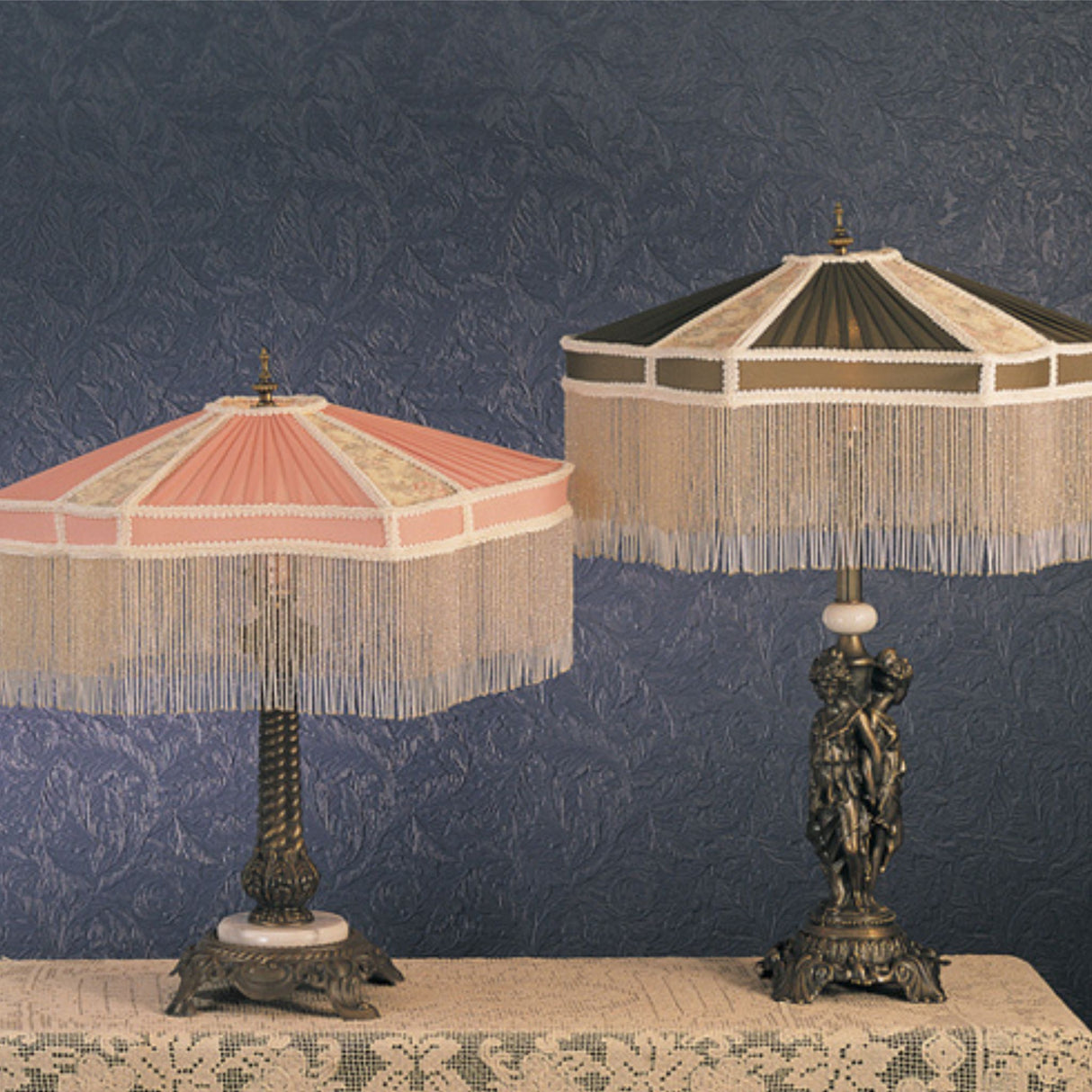 Pair of Persian table lamps with fabric and fringe shades in pink and green, placed on an ornate table.