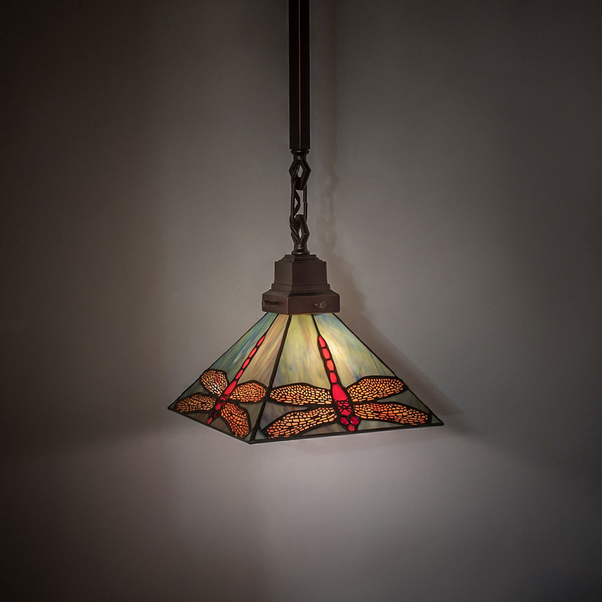 Prairie Dragonfly Pendant illuminated in a dark background, enhancing its vibrant hues.