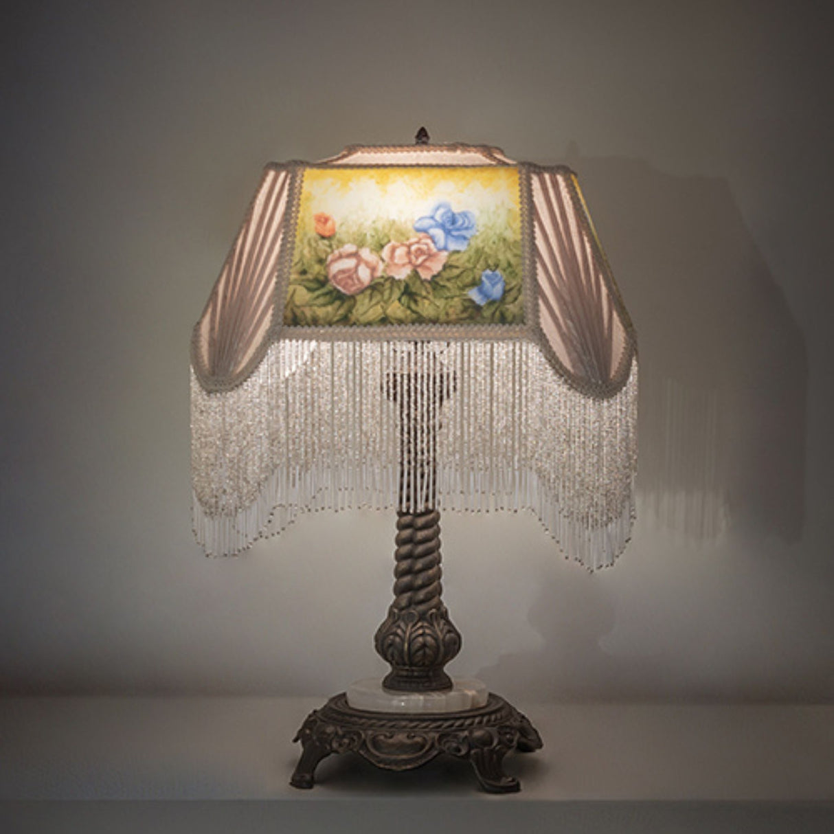 Reverse painted roses table lamp with ornate base and fringed shade.