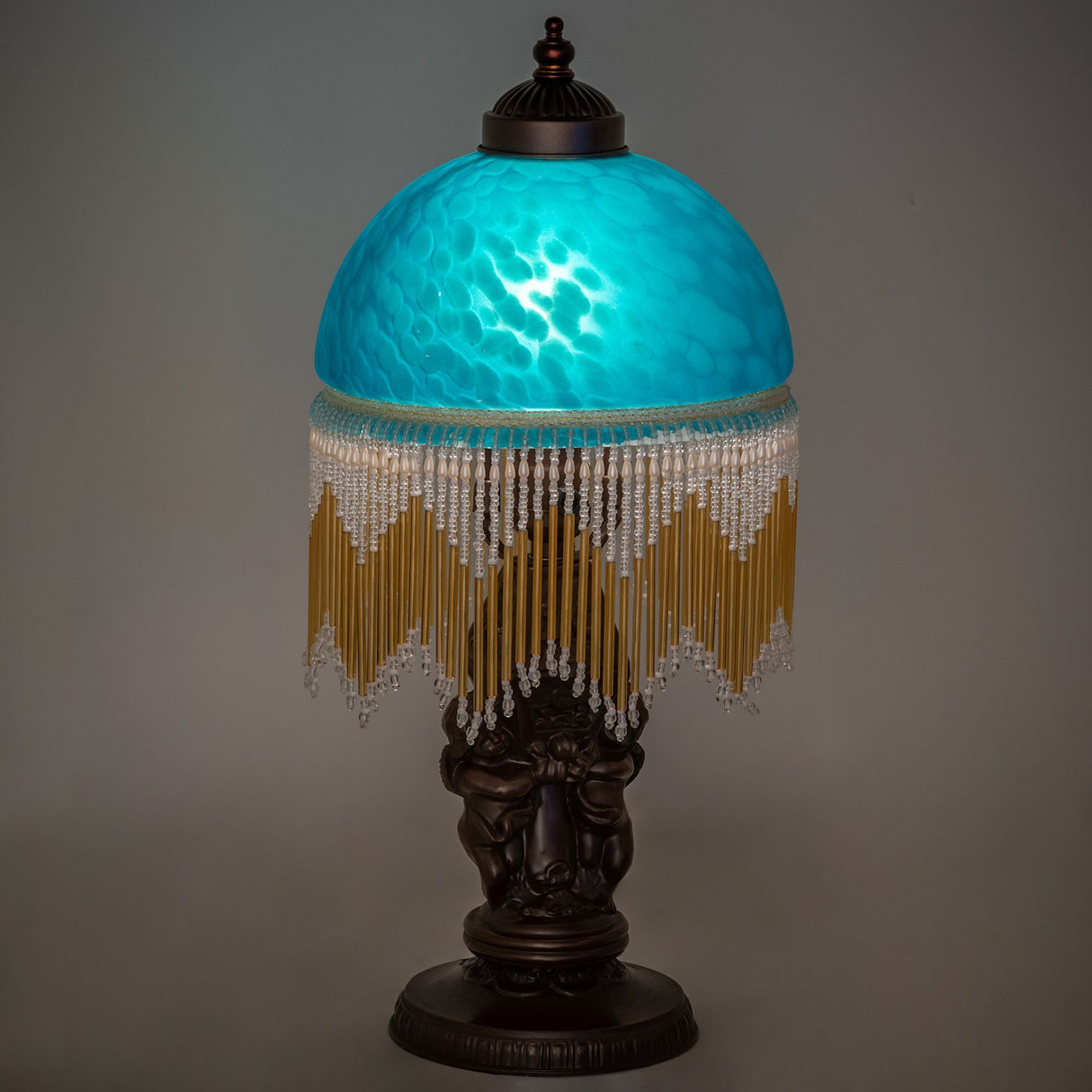Illuminated, showcasing its teal mottled glass shade and elegant beaded fringe.