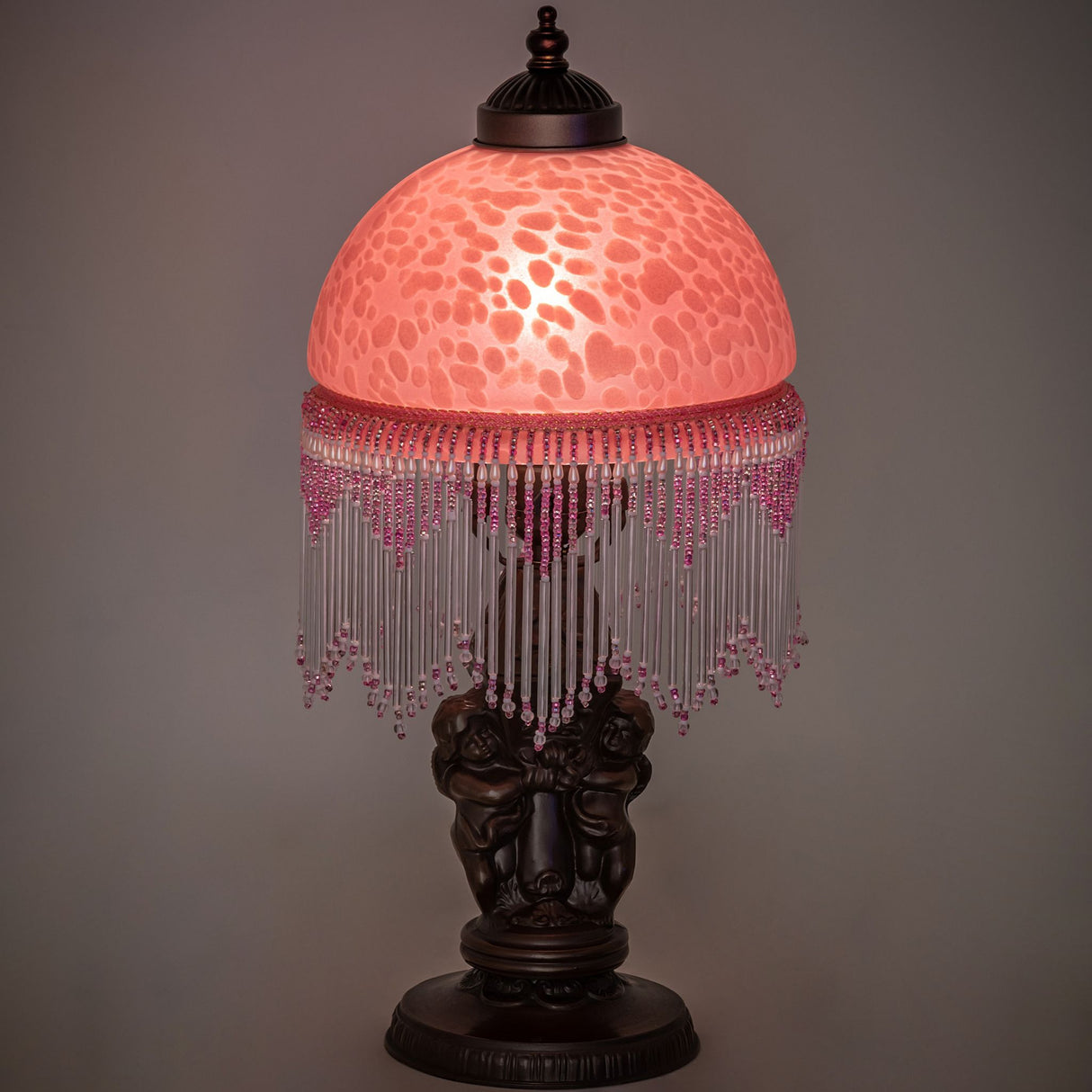 Illuminated, highlighting its Cranberry Mottled Glass shade and intricate cherub base.