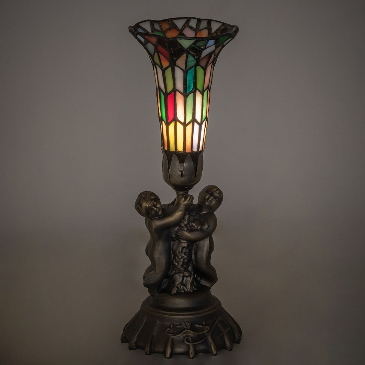 Ambient view of twin cherub lamp with warm stained glass glow.