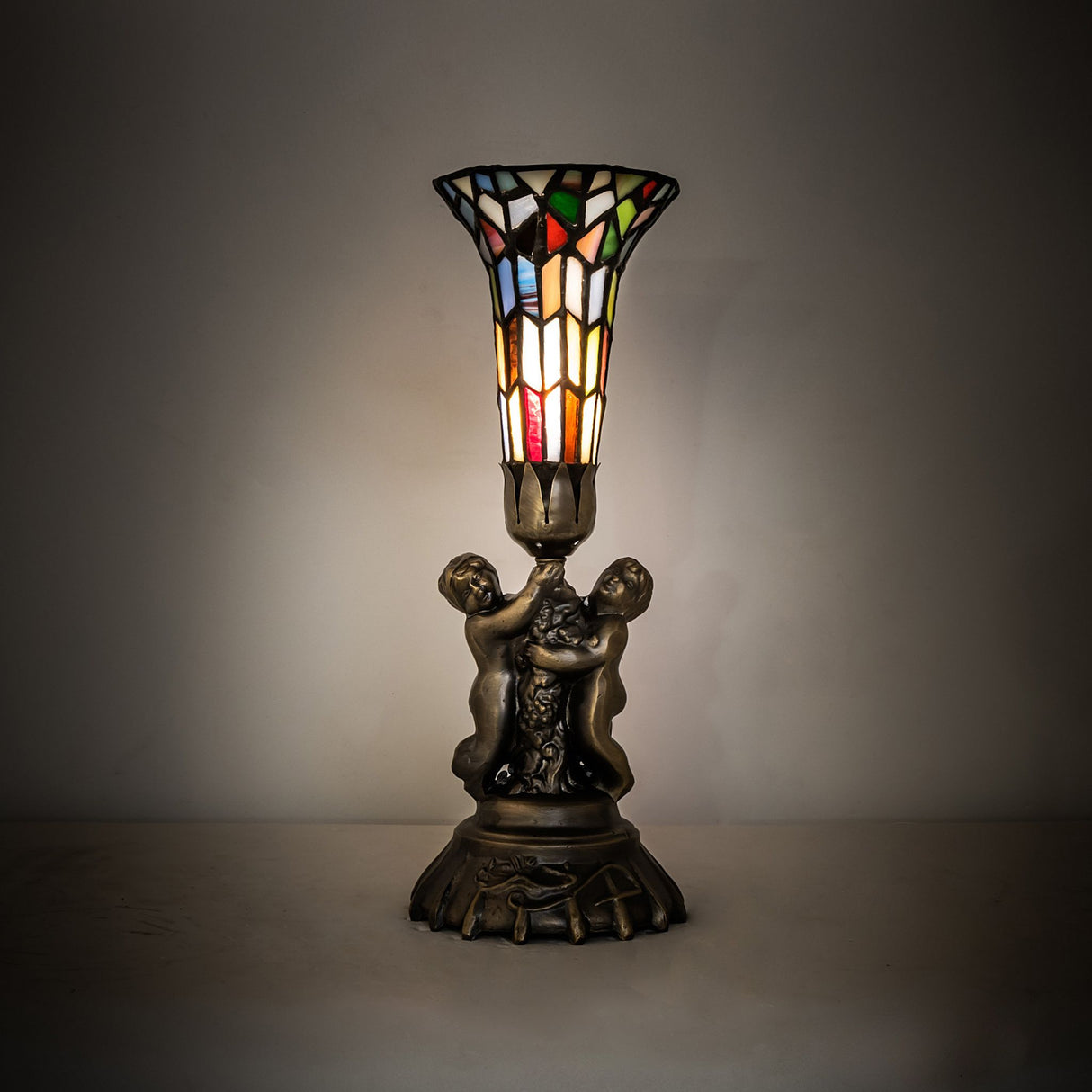 Stained glass twin cherub lamp glowing in ambient lighting.