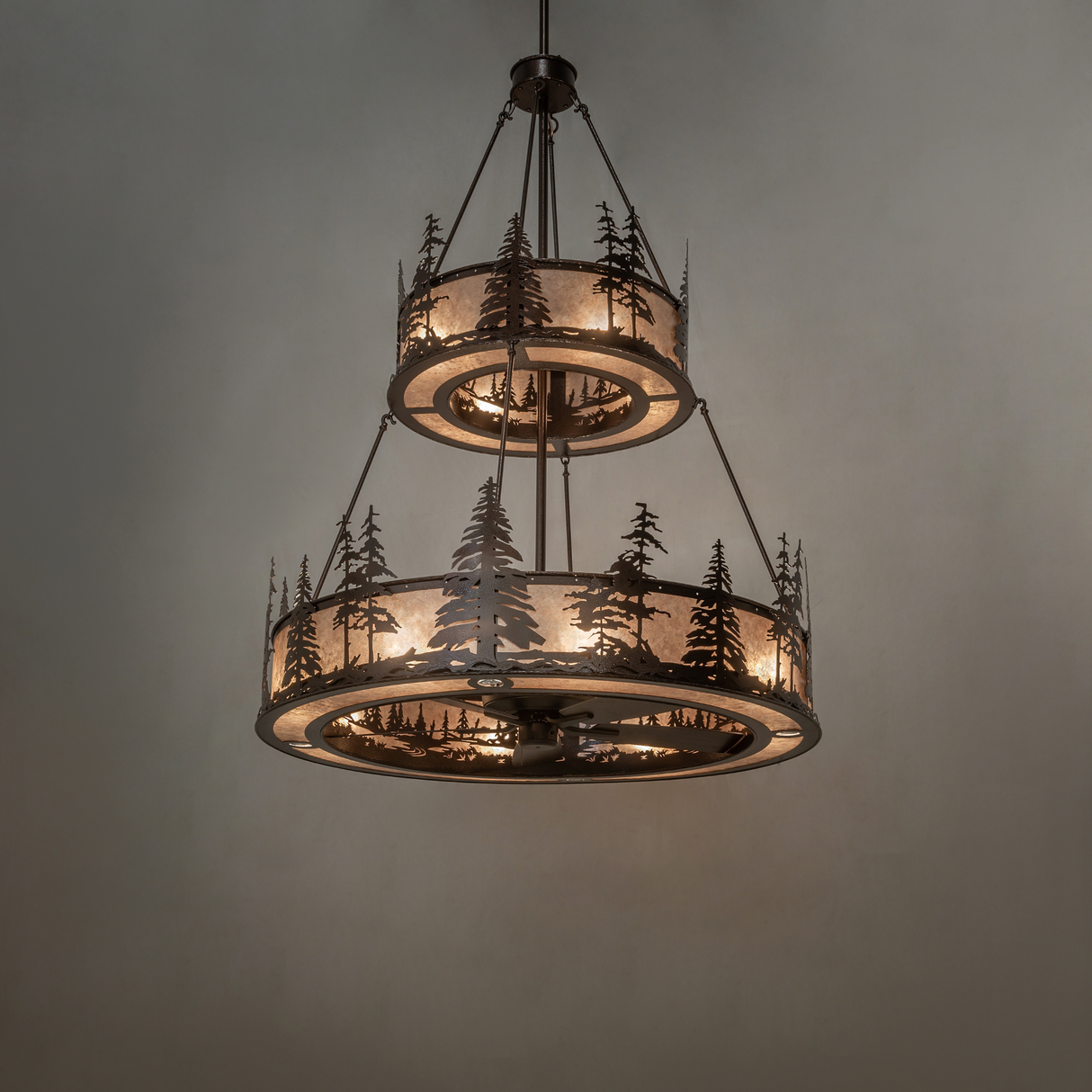 Warm glowing Tall Pines chandelier fan with layered pine tree pattern.
