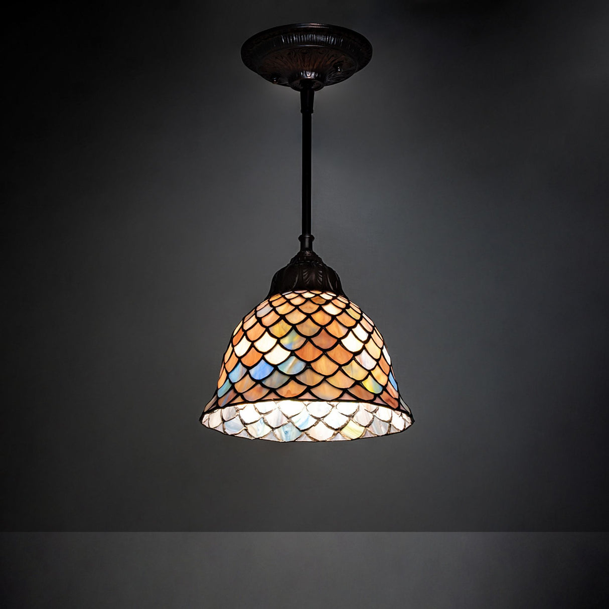 Illuminated Tiffany Fishscale mini pendant casting a warm glow in Mahogany Bronze.