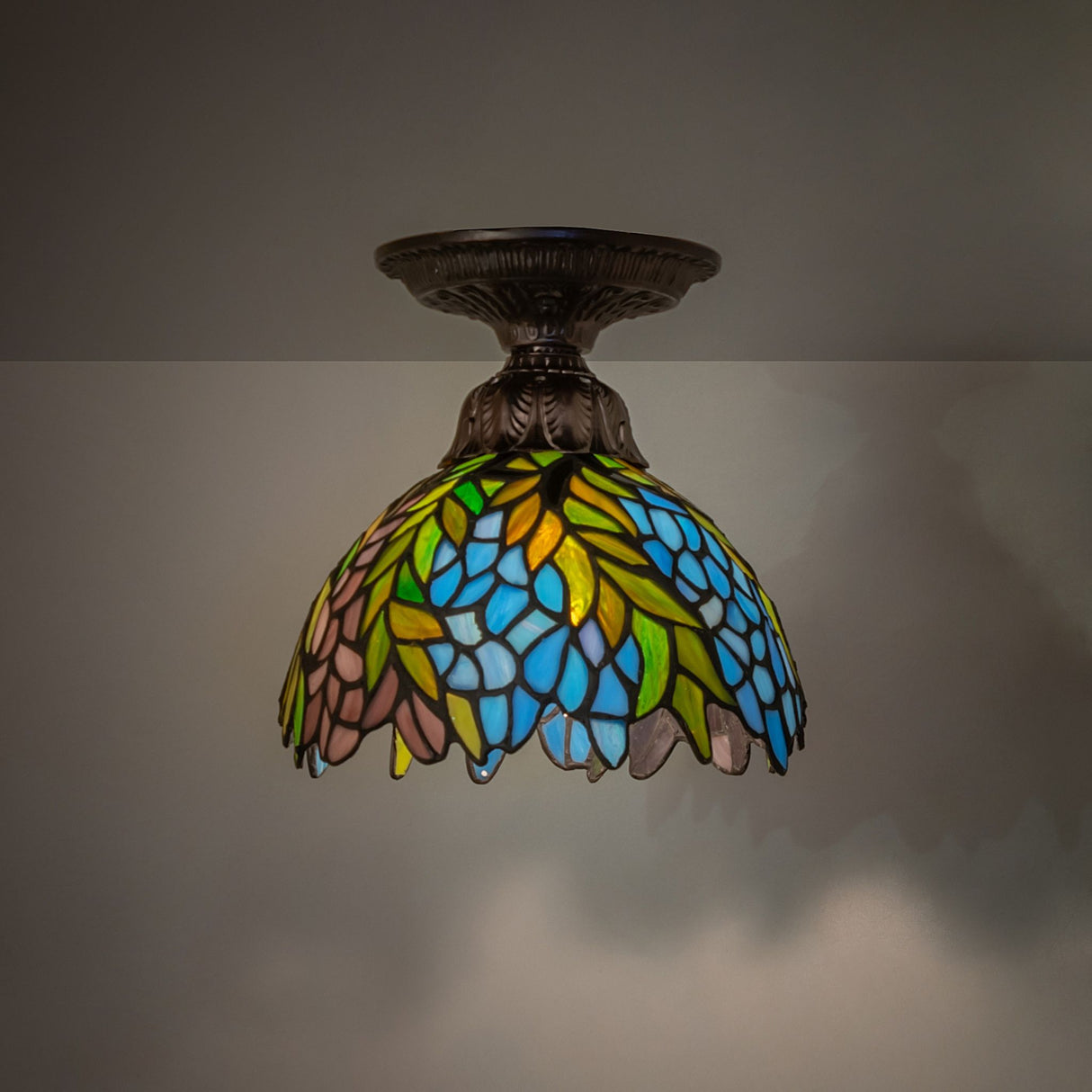 illuminated dark view of tiffany honey locust flushmount with vibrant stained glass colors.
