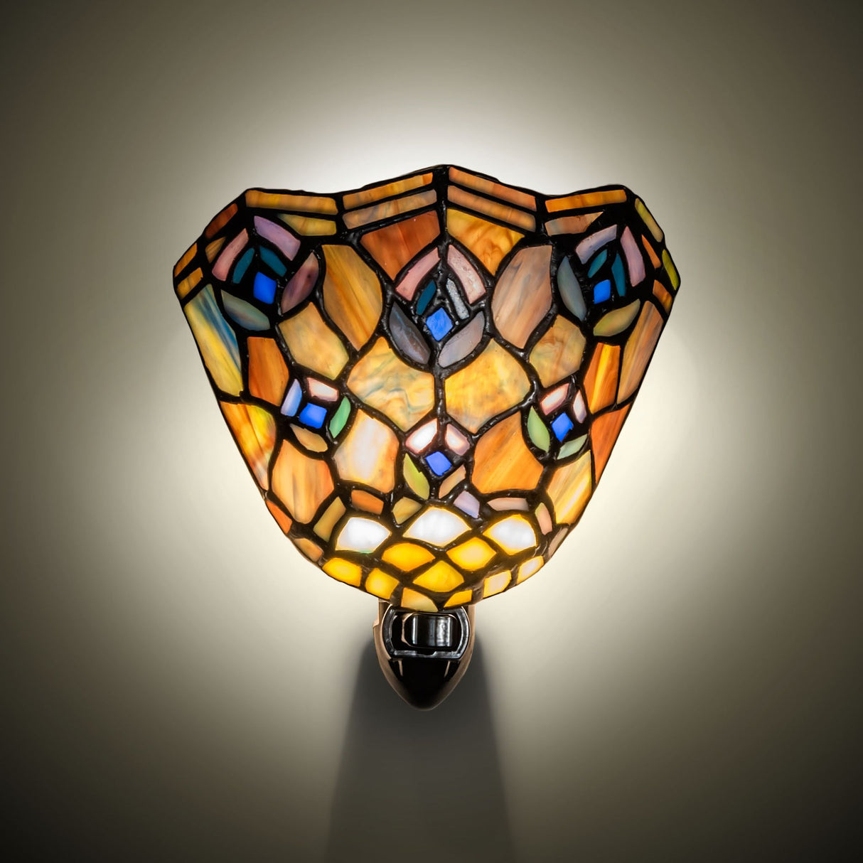 Ambient view of Tiffany Peacock Feather night light glowing with warm stained glass colors on wall.