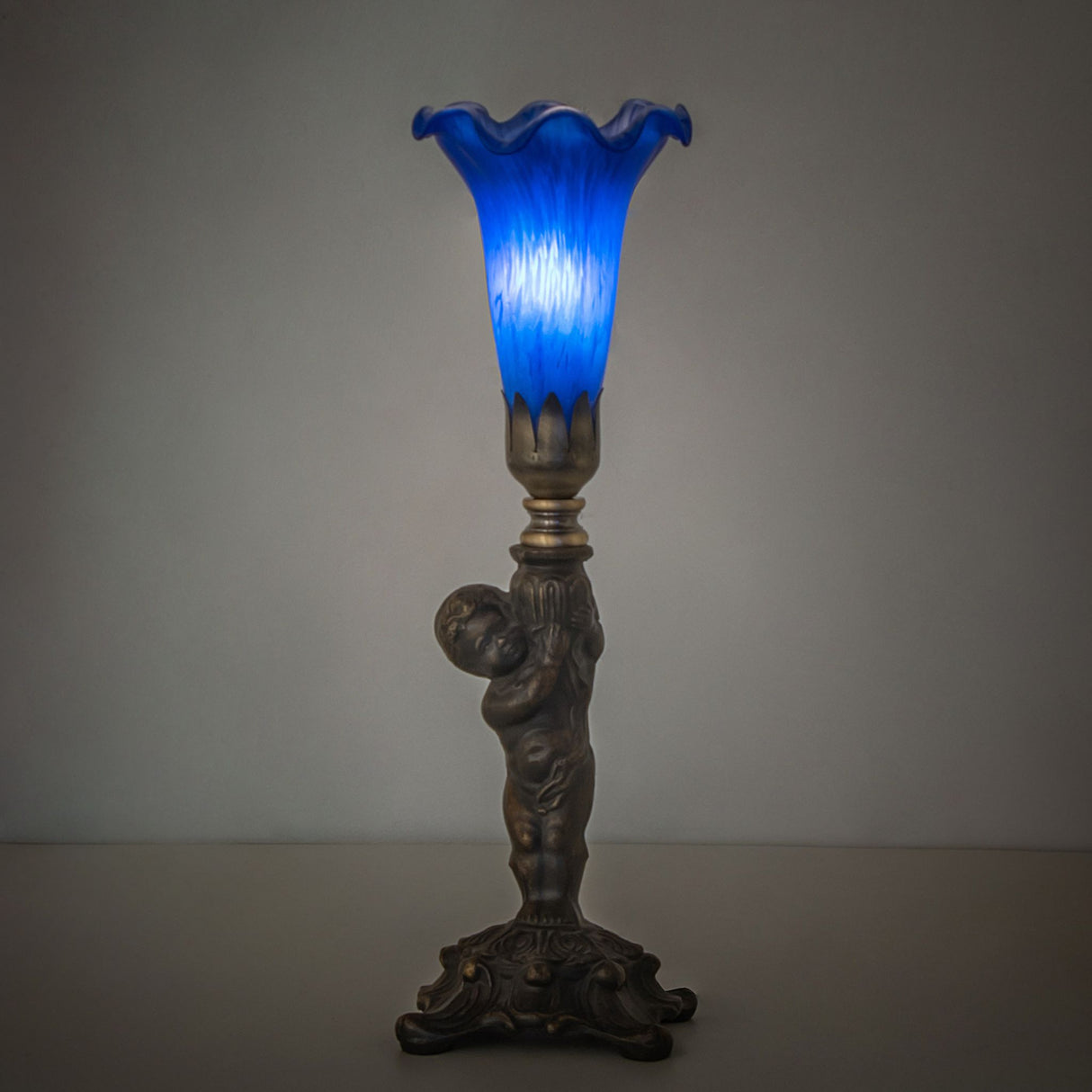 Ambient view of the Blue Tiffany Pond Lily Cherub Mini Lamp, softly glowing in a dim setting.