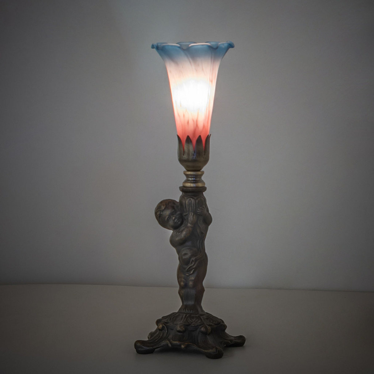 Pink and blue Tiffany cherub lamp illuminated.