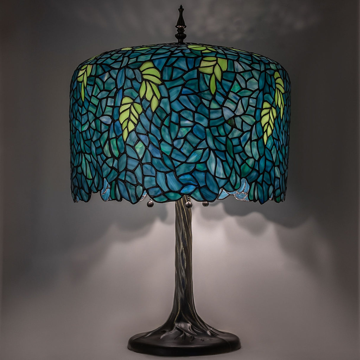 Tiffany Wisteria table lamp illuminated with intricate blue-green stained glass.