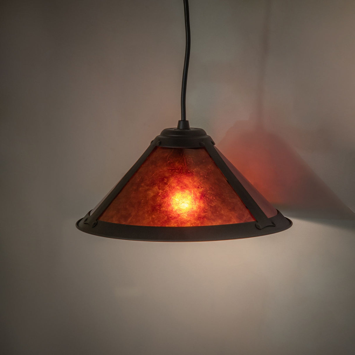 Warm amber glow emanating from a cone-shaped Sutter pendant light with a rustic finish.