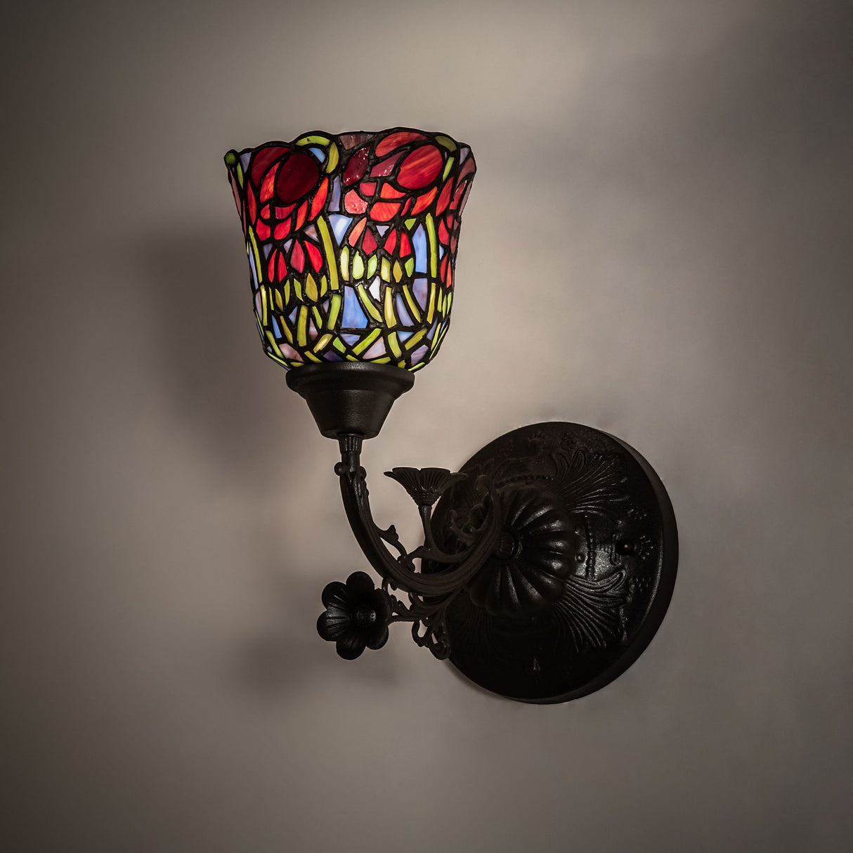 Red rosebud wall sconce illuminated, showcasing its vibrant stained-glass design.