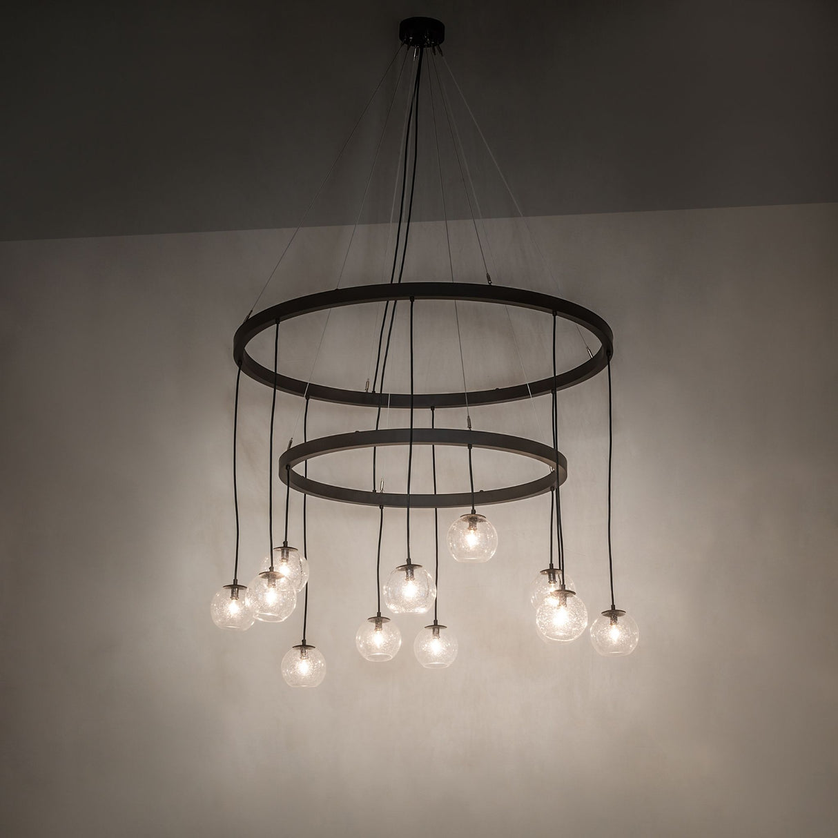 Ambient room view of lit Bola 12 light 2 tier chandelier with cascading clear glass orb pendants.
