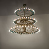 Ambient view of 108-light chandelier glowing in room with brushed brass and copper tiers.