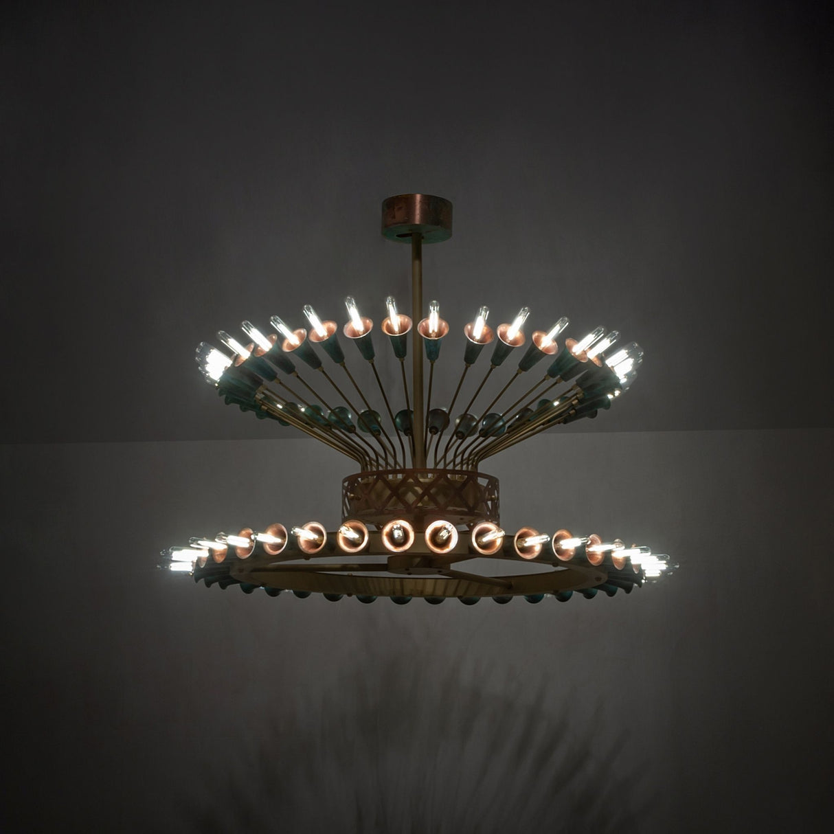Coyle 72 light two-tier chandelier glowing in room setting with brass and verdigris copper details.