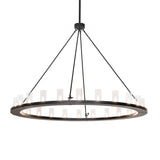 Lit view of chandelier, featuring 24 clear glass cylinders on a circular black metal frame.