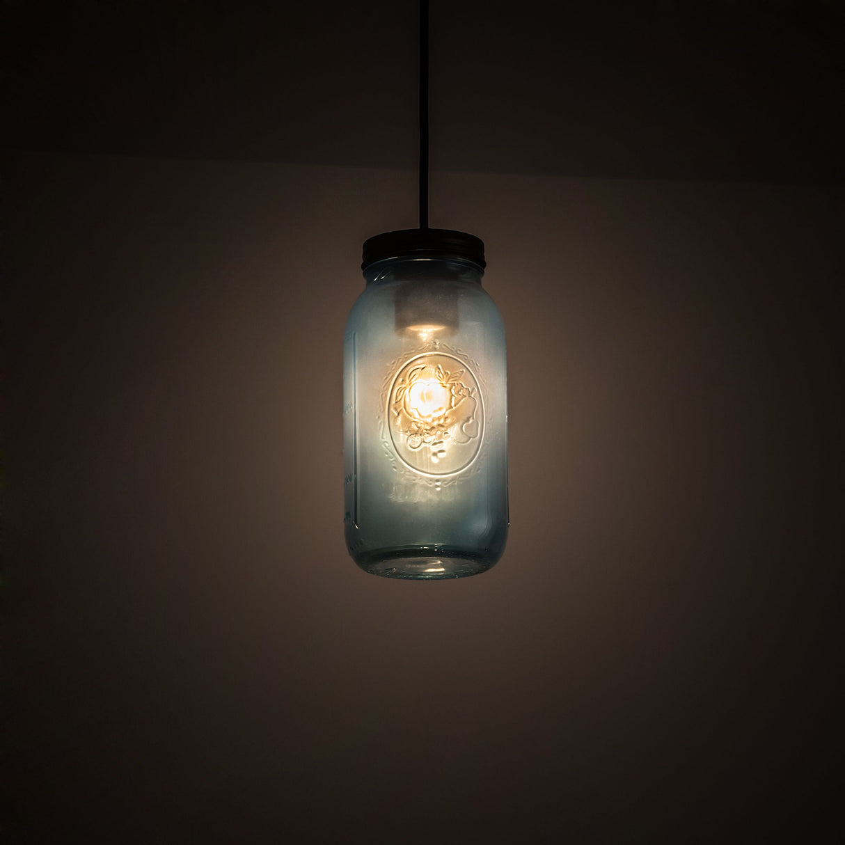 Glowing blue Mason jar pendant in a dark room.