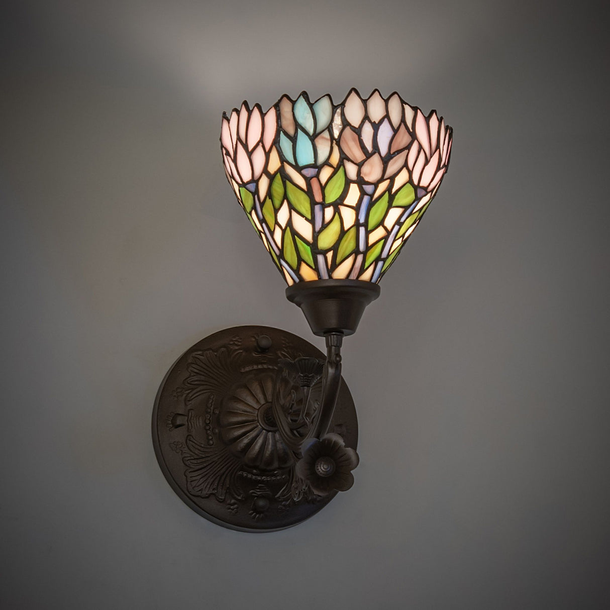 Illuminated Wisteria wall sconce mounted on a wall, floral pattern glowing.