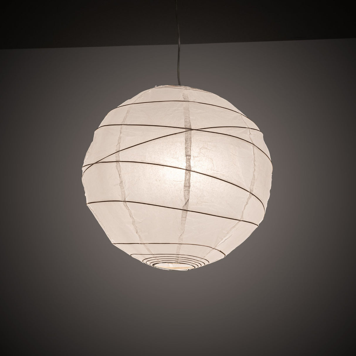 Illuminated paper lantern pendant in a dark room.
