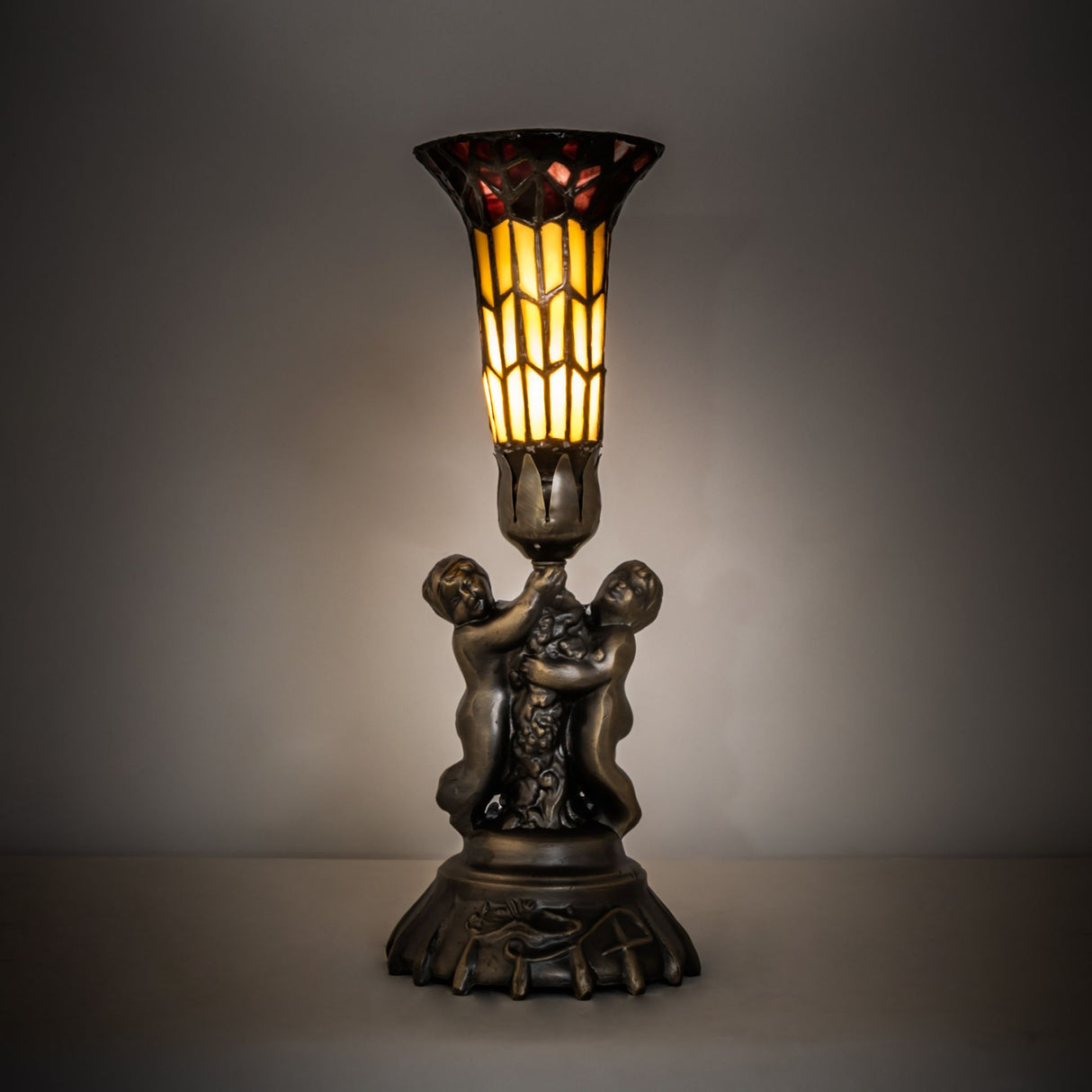 Lit view of the Pond Lily Twin Cherub accent lamp with amber and red glass shade.