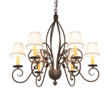 Lit view of 6-light chandelier with off-white shades glowing, gilded tobacco finish.