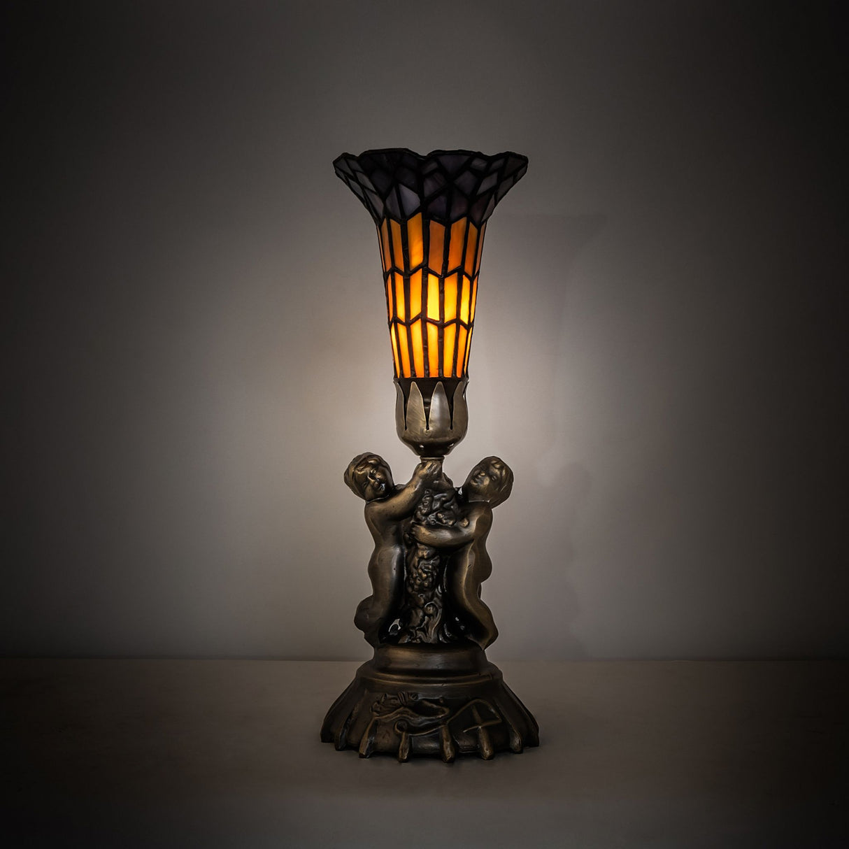Illuminated view of stained glass pond lily twin cherub accent lamp glowing warmly.