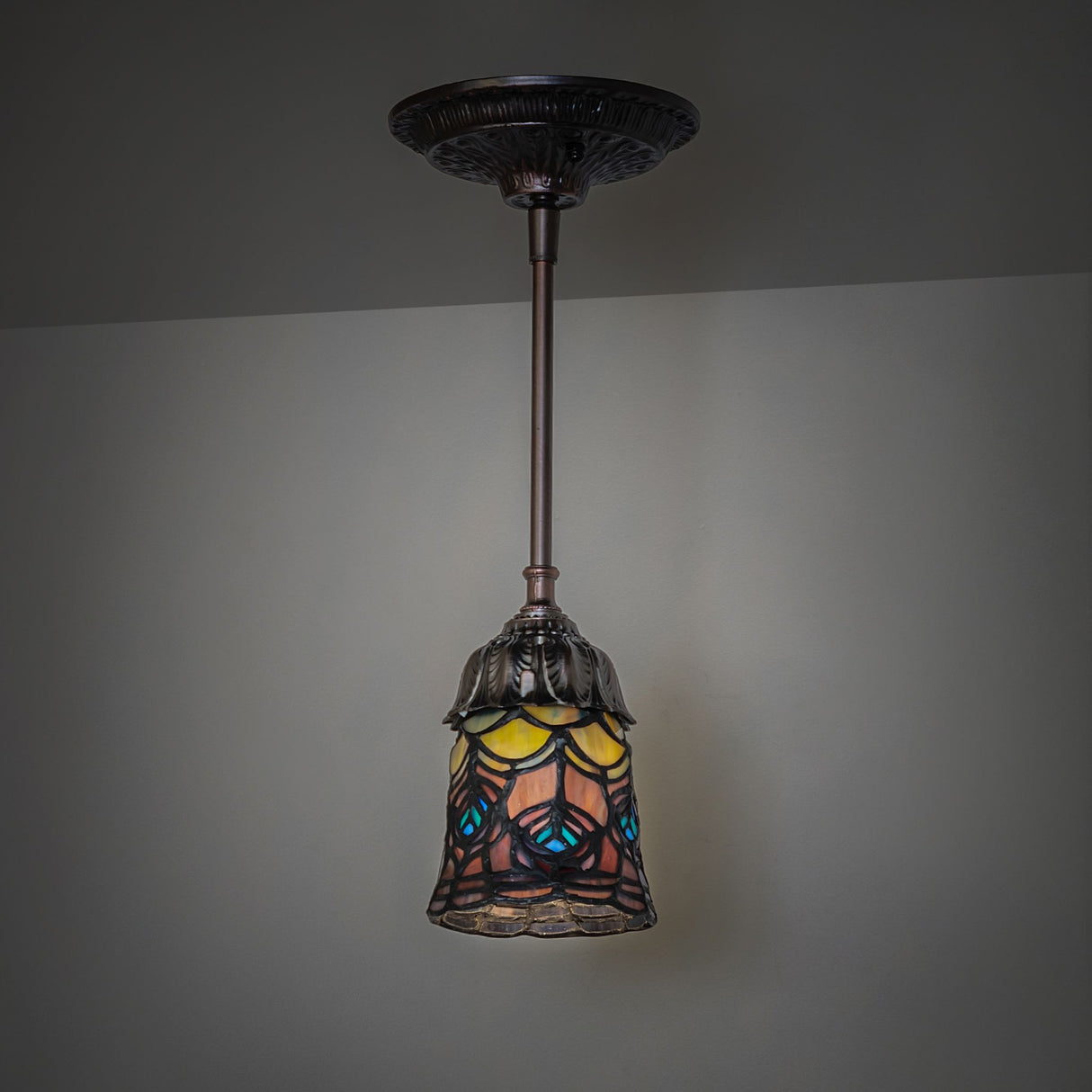Dark room ambiance with Tiffany Peacock Feather Mini Pendant emitting warm light.