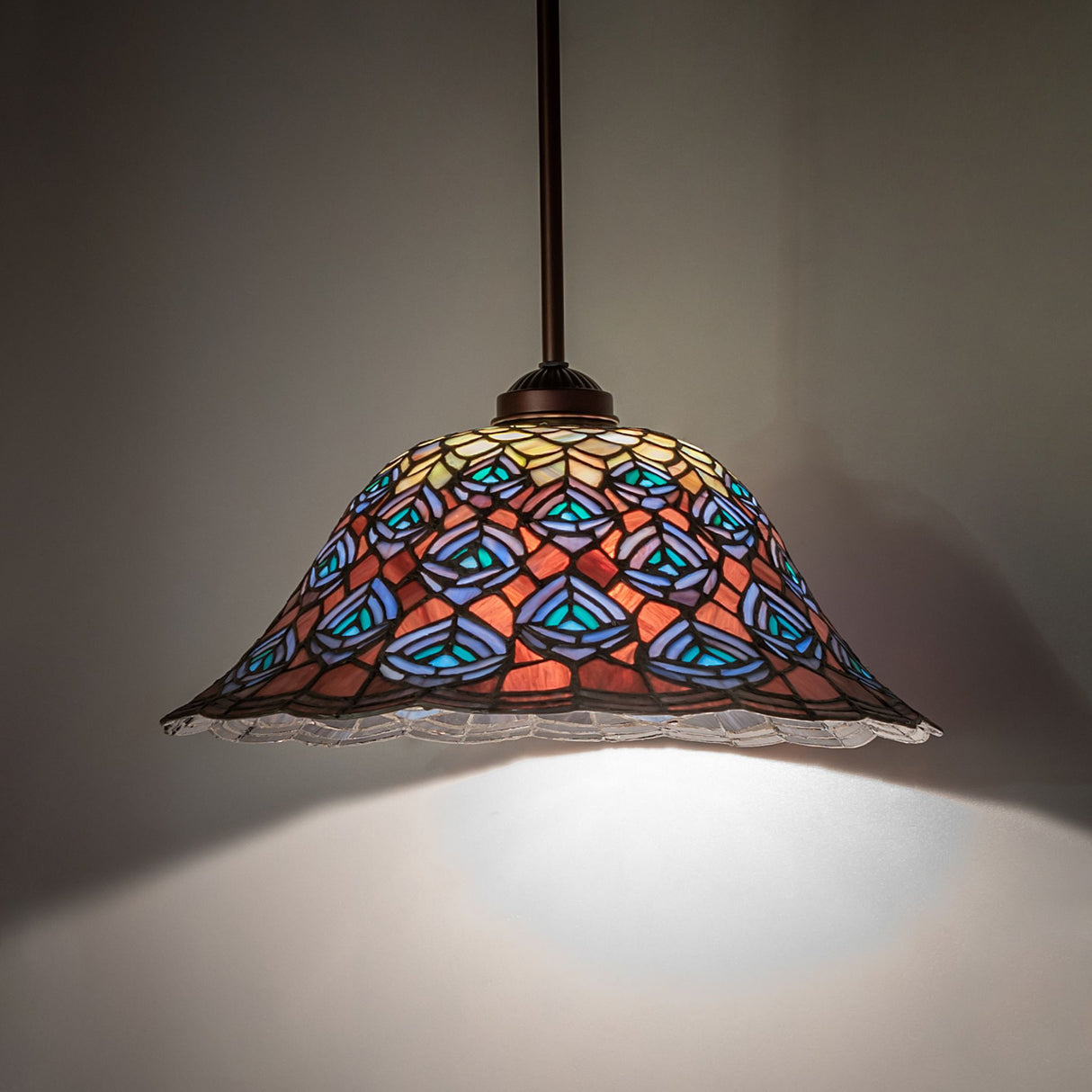 Illuminated Tiffany Peacock Feather Pendant, showcasing its vibrant glow and detailed stained glass.