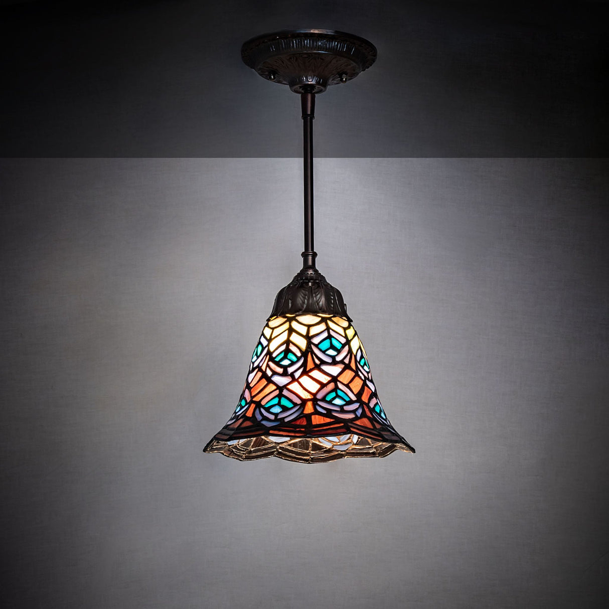 Illuminated Tiffany-style peacock feather pendant glowing warmly.