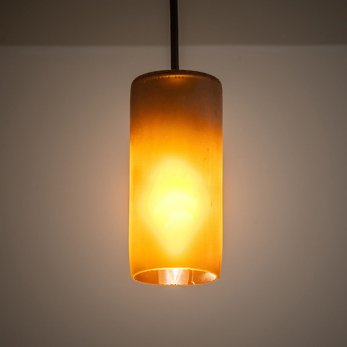Venice Frosted Amber Wine Bottle Mini Pendant glowing softly against a wall.