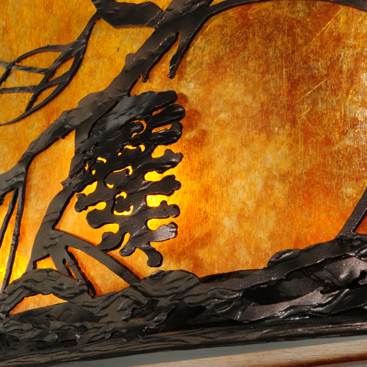 Close-up of pine branch metalwork and glowing mica shade.